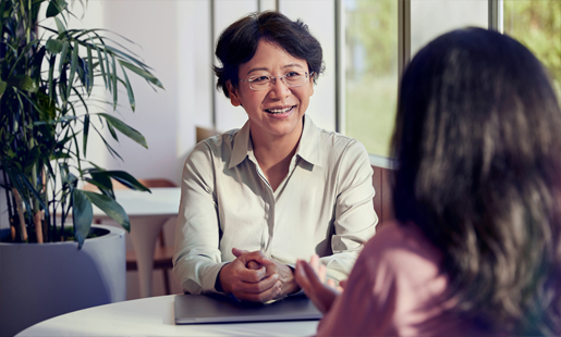 Jean istuu työkaveriaan vastapäätä ja hymyilee.