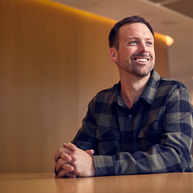 Jordan istuu ja hymyilee. Hän on on laittanut kädet ristiin eteensä.