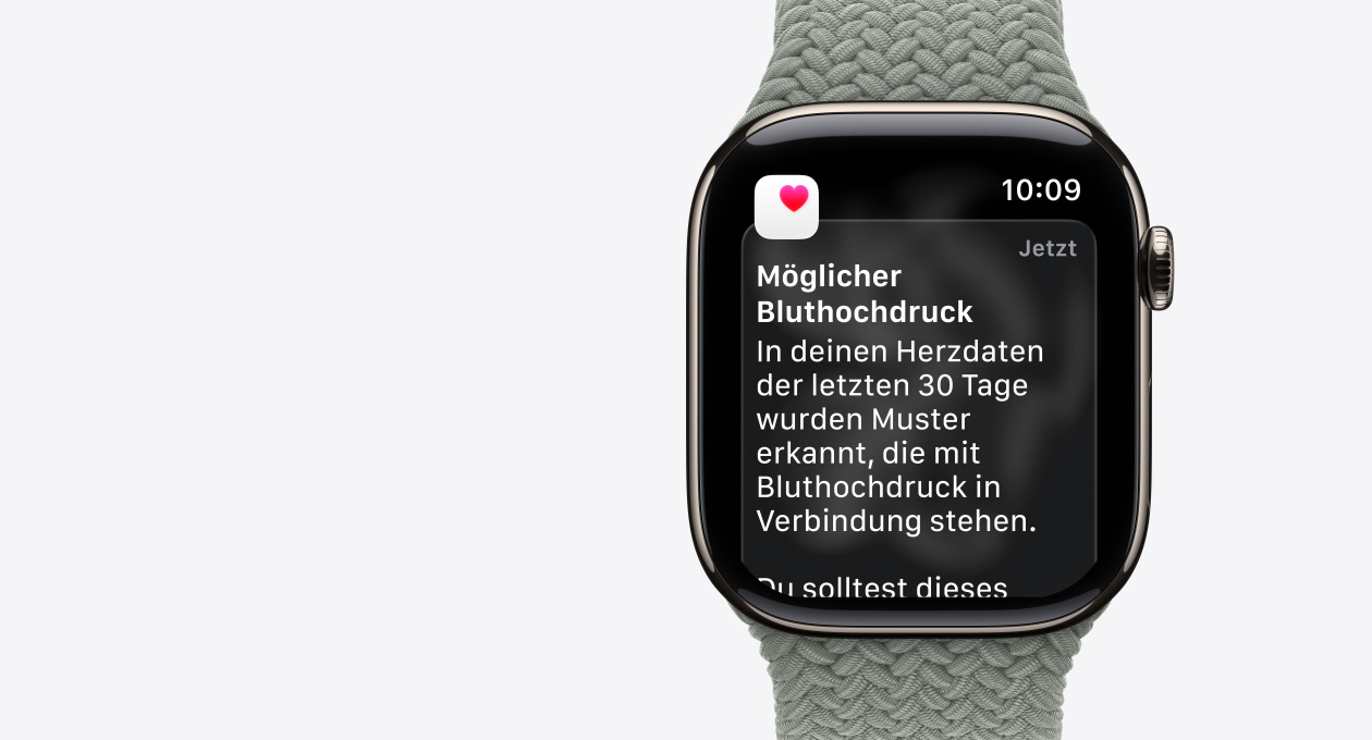 Apple Watch Series 11, Farbe Gold, Titangehäuse, Mitteilung: Möglicher Bluthochdruck, pinkes Herz in weißem Feld, rechte Seitenansicht, Digital Crown, Armband, Geflochtenes Solo Loop Grüngrau