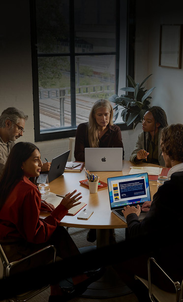 Cinco pessoas sentadas à volta de uma mesa de conferência, a colaborar em computadores MacBook, com os iPhone virados para baixo