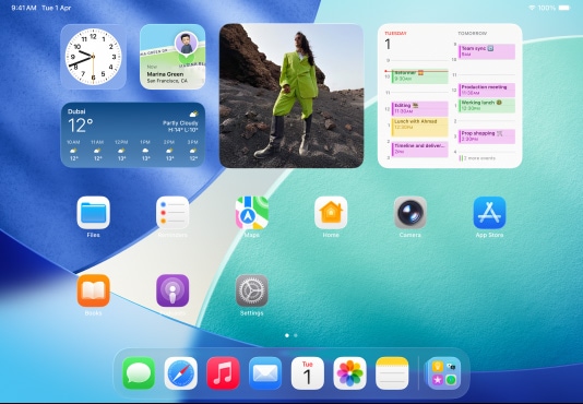 iPad, three models, landscape orientation, with center model in front of two others, Apple Pencil magnetically attached to top of center model, center screen showing the Home Screen featuring colorful app icons with Liquid Glass effect, left screen showing the Preview app, right screen showing Home Screen with files fanning out from the dock