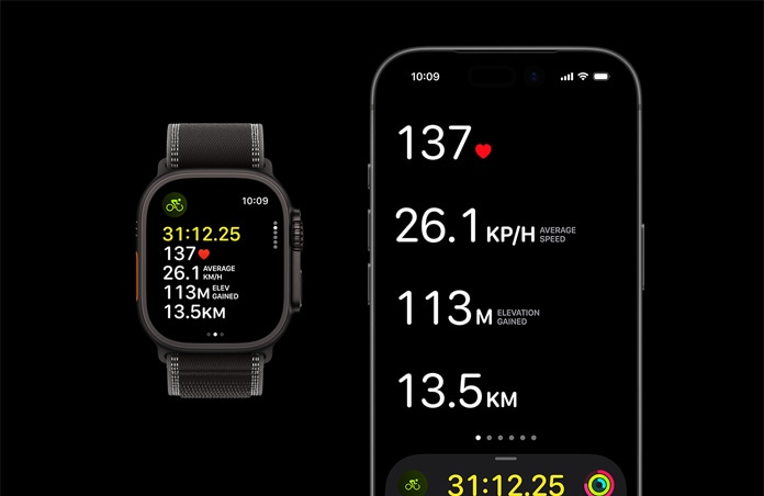 Apple Watch Ultra 3 у титановому корпусі чорного кольору з браслетом Trail чорного/попелястого кольору поруч з iPhone, активні показники тренування відкриті на обох пристроях