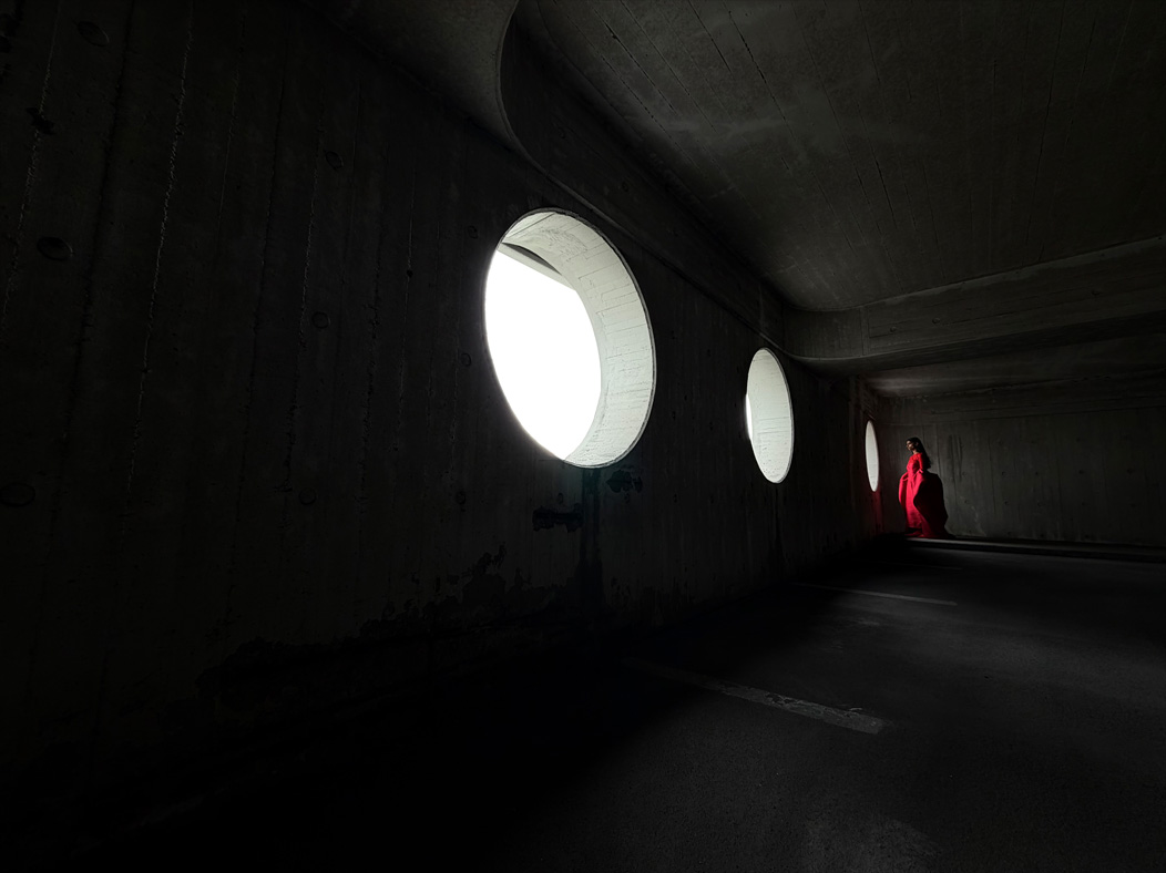 Une femme vêtue d’une longue robe rouge se fait photographier dans une pièce vide. L’app Appareil photo change de distance focale pour illustrer les capacités du système caméra pro, mettant en valeur : 13 mm