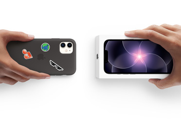Mano que sujeta un iPhone 11 con una funda de silicona con pegatinas en la parte trasera, al lado de una mano que sujeta la caja de un nuevo iPhone 17e