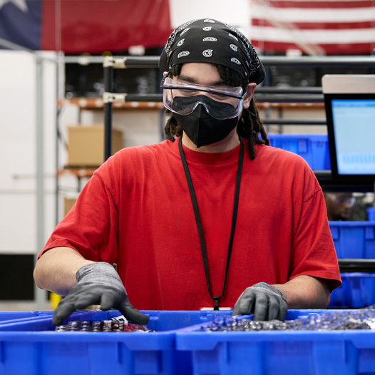 An employee wearing safety gloves, glasses, and mask handles materials at a facility